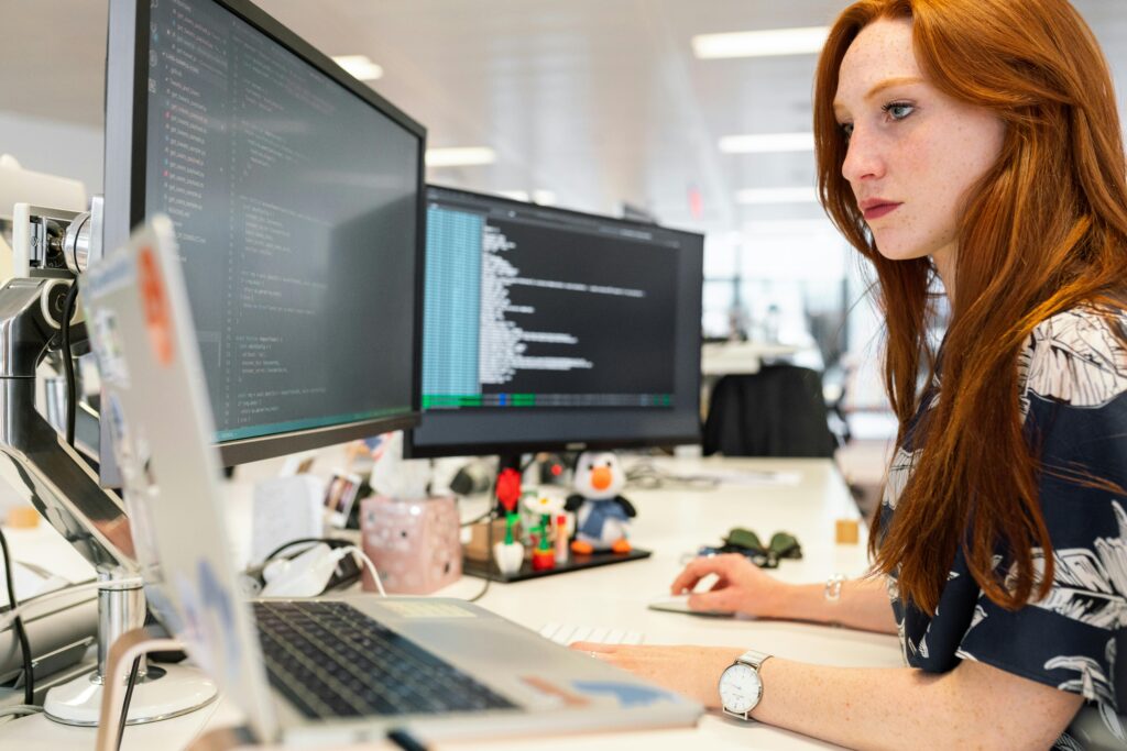 A focused female software engineer coding on dual monitors in a modern office.